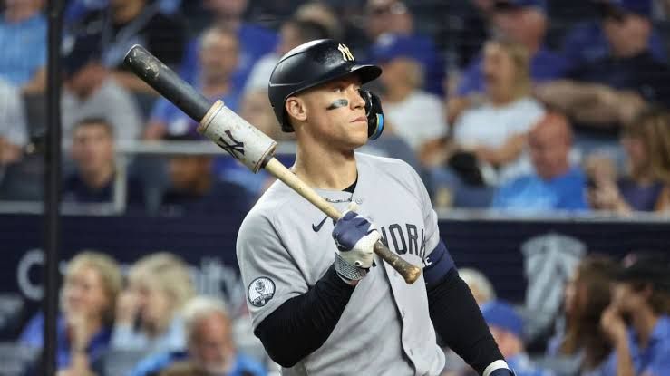 Aaron Judge walking toward the dugout during a game at Yankee Stadium while wearing a team jersey.