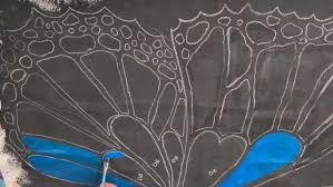 Artist Melanie Therrien painting butterfly wings on a surface to cover graffiti in Lewiston.