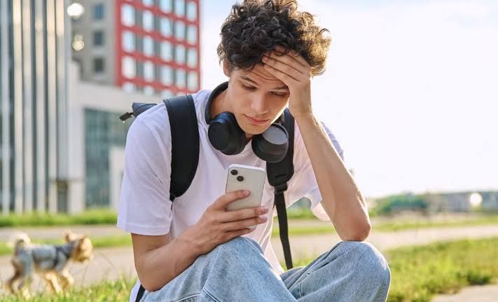 Close-up of a college student looking at a smartphone screen while sitting on a campus bench.
