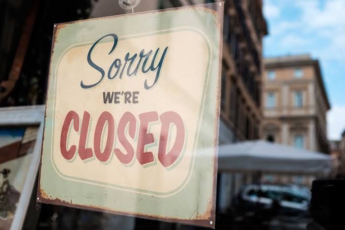 A physical storefront with a closed sign hanging on the front door representing business inactivity.