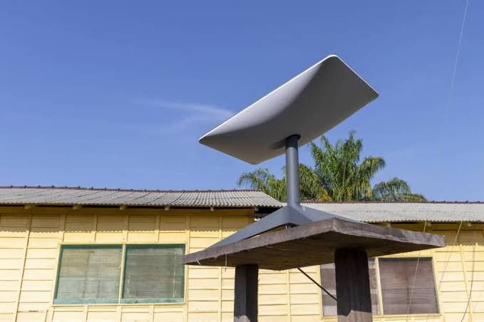 A technician checking signal strength on a satellite dish mounted to the roof of a remote rural residential building.