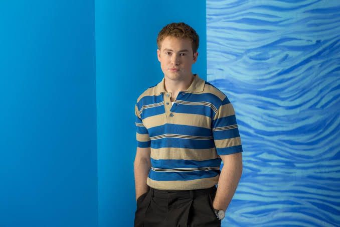 Kit Connor posing for a studio portrait against a blue background.