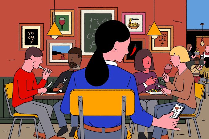 A person looking at a food tracking app on their phone while eating with friends at a dinner table.