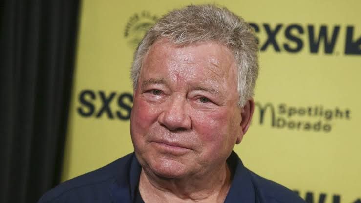 William Shatner stands on a stage holding a microphone during an entertainment event in Chicago.
