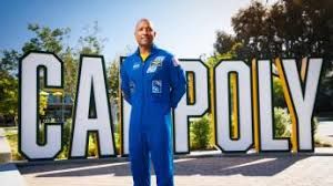 Astronaut Victor Glover in his flight suit standing at a podium at a Cal Poly press event.