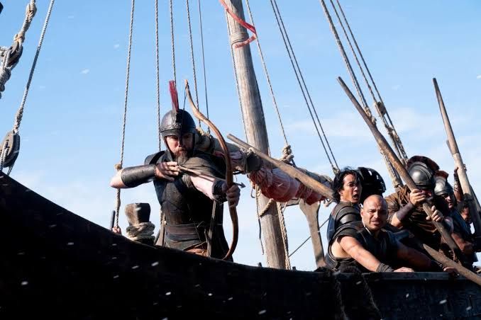 Matt Damon portrays Odysseus holding a bow while standing on the deck of a ship in a scene from The Odyssey.