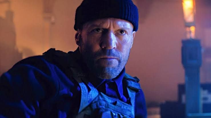 Jason Statham walking on a film set, looking focused during the production of his latest action movie.