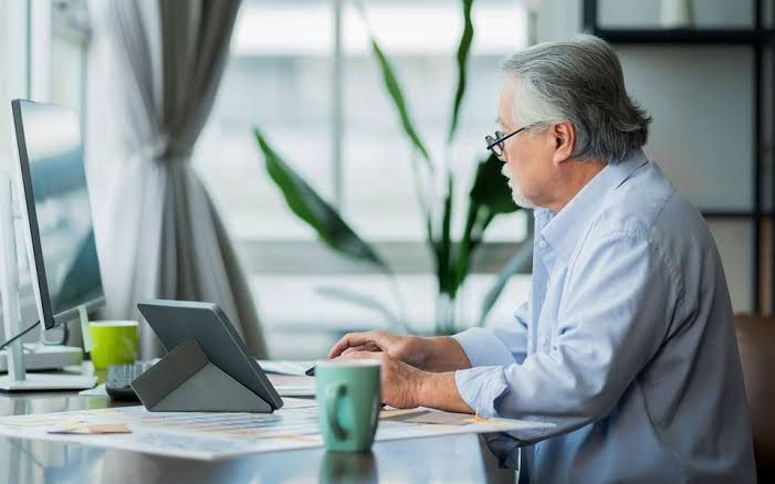 An elderly worker in a professional setting looking at documents in a Greek office context.