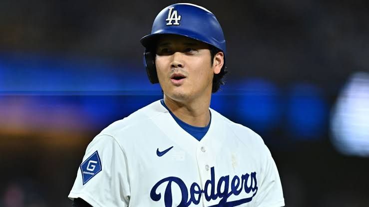 Shohei Ohtani standing in the Dodgers dugout watching his teammates during a game.