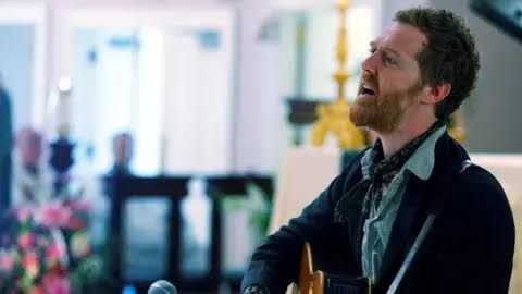 Glen Hansard holding a guitar and performing on stage during a concert.