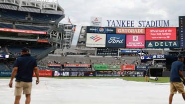 Yankee Stadium field during a rain delay with empty seats and covered infield dirt.