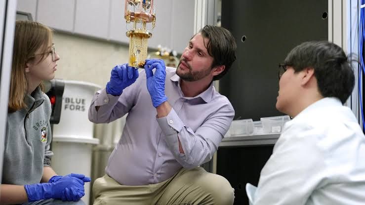 Nik Zhelev stands in the University of Oregon lab next to a dilution refrigerator used for quantum training.