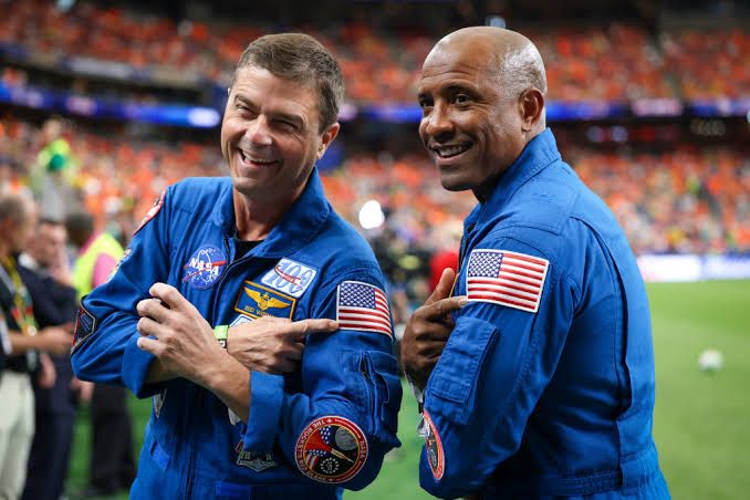 Artemis II commander Reid Wiseman and pilot Victor Glover posing in NASA flight suits before their mission.