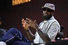 LeBron James sitting on a stage wearing sunglasses and a cap while speaking at Fanatics Fest.