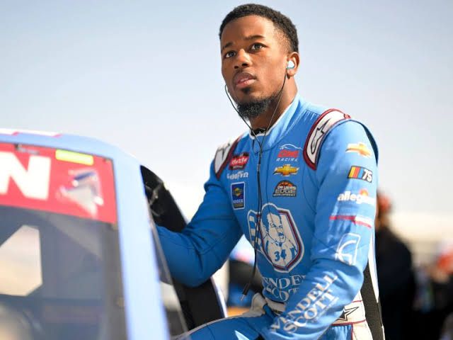 NASCAR driver Rajah Caruth standing in his racing suit near his No. 88 vehicle during the 2026 racing season.
