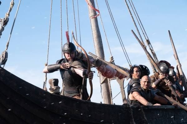 Matt Damon as Odysseus in The Odyssey, directed by Christopher Nolan, posing with a bow in a scene from the film.