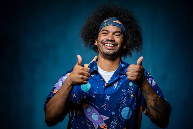 Mychal Threets in a blue shirt with his thumbs up, posing for a photo.