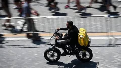A Glovo delivery rider cycles through the Imperial Forum in Rome during a hot summer day.