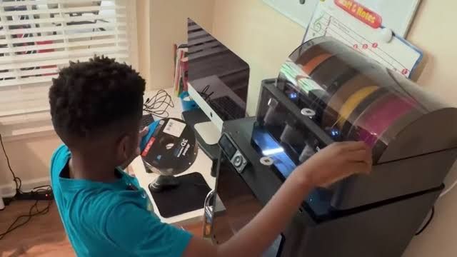 Twelve-year-old Aaron Osirus operating a 3D printer to create custom toys in his home playroom.