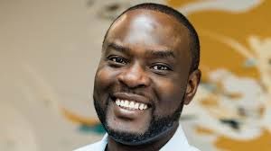 Founder Shegun Otulana standing in a bright office space discussing venture studio growth and Birmingham tech development.