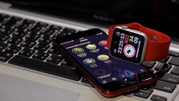 Close-up of an iPhone SE and a silver Apple Watch with a red band sitting on a desk.