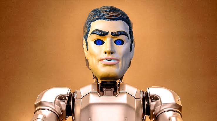 A metallic robot wearing a human mask against a copper background, representing AI human-like behavior.