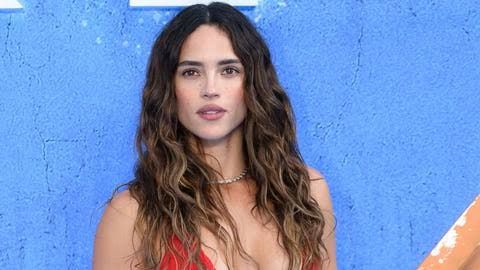 Adria Arjona attending a formal industry event while the DC Studios logo appears in the background.