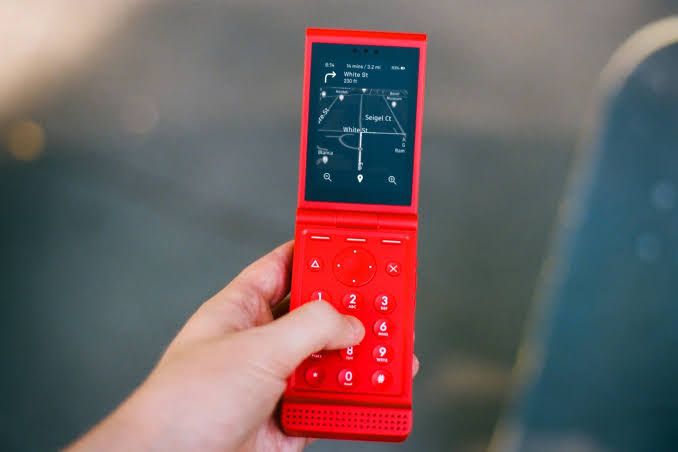 A yellow Light Flip phone standing on a wooden surface with a single glowing notification light on the corner.