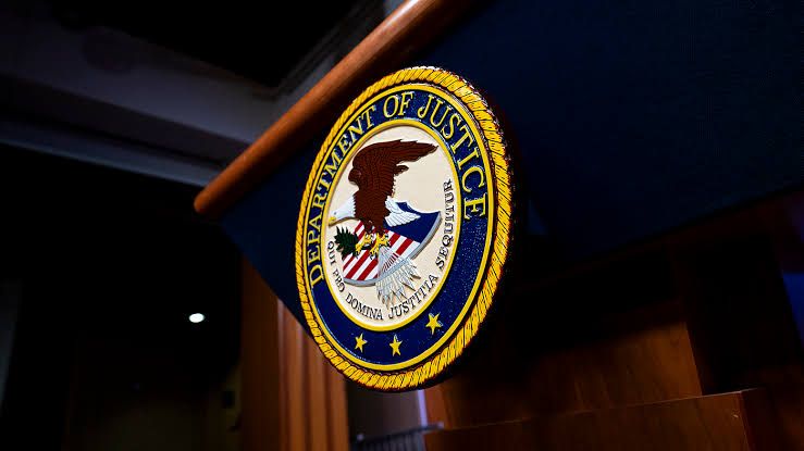 A close-up view of Department of Justice branding displayed on a digital screen during a press conference.