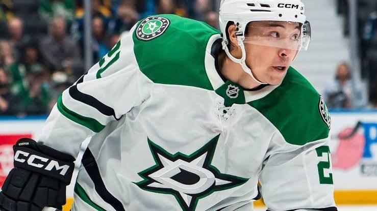 Jason Robertson in a Dallas Stars jersey during an NHL game, looking for an open teammate on the ice.