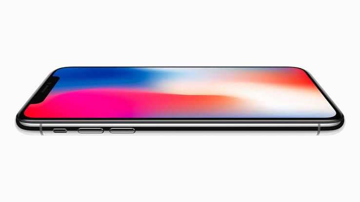 iPhone X displayed on a table next to modern smartphone components in a tech laboratory setting.