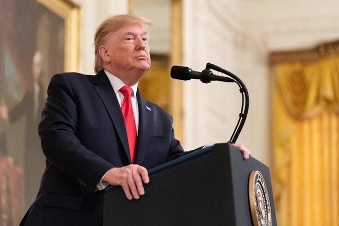 President Donald Trump speaking from a podium at the White House with a flag in the background.