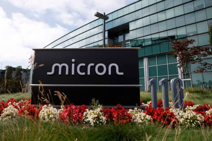 Micron Technology logo displayed on a clean office wall behind a blurred modern server room entrance.