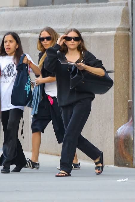Ashley and Mary-Kate Olsen walking on a New York sidewalk in black and white transitional outfits.