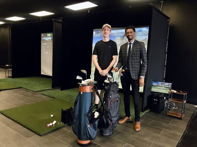 Steven Cox and Jarrett Osterhout stand in front of two TruGolf simulator bays inside the new ReviveZone center.