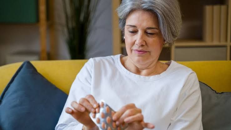 Woman holding statin pills while reflecting on heart health.