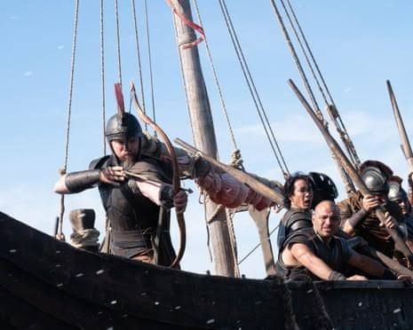 Matt Damon filming a battle scene from The Odyssey as a warrior with a bow on a wooden ship.