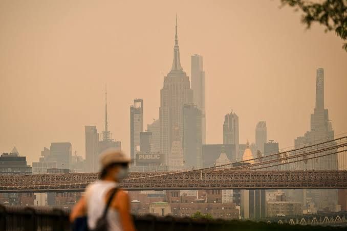 A person wearing a face mask walks near the Brooklyn Bridge during hazy conditions caused by Canadian wildfire smoke.