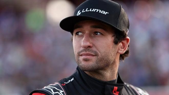 Chase Elliott standing near his NASCAR stock car at a racetrack during a race weekend.