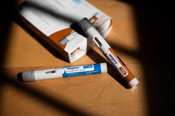 A close-up of a Wegovy injection pen held by a medical professional in a clinical setting.