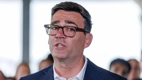 Andy Burnham in a suit and glasses looking toward the camera during a press briefing.