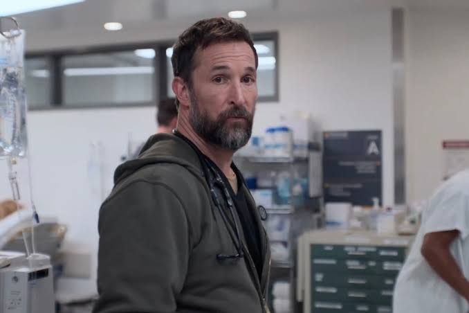 Noah Wyle standing in a hospital hallway wearing scrubs while looking distressed during the filming of The Pitt.