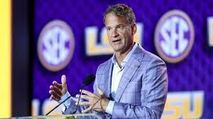 Lane Kiffin standing on the sideline at a football stadium while wearing a white shirt and headset.