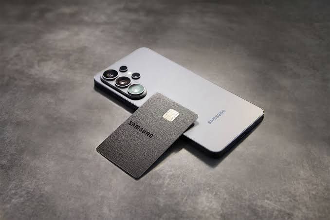 Samsung Galaxy Card sitting on a table next to a folded smartphone and a cup of coffee.