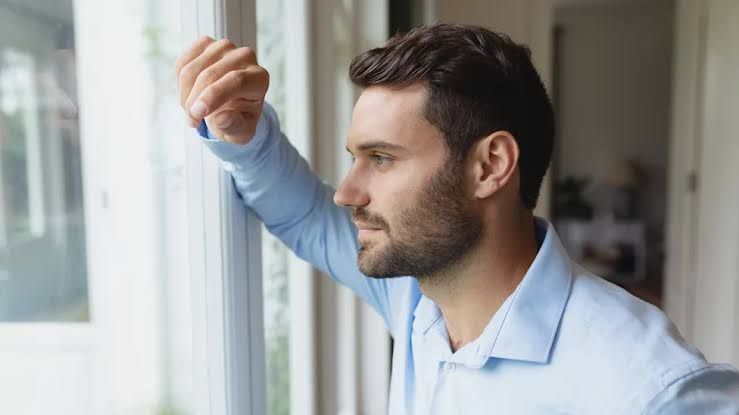 A man looking visibly tired while sitting on a bed in the morning, representing physical symptoms of depression.
