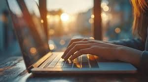 Close up of hands typing on a laptop keyboard in a home setting.