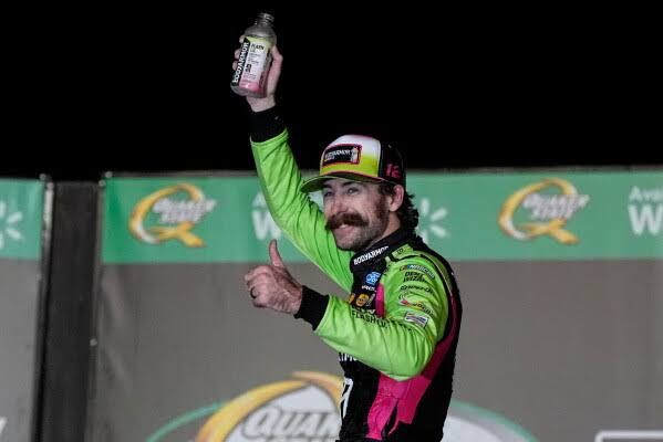 Ryan Blaney celebrating his NASCAR Cup Series victory at Atlanta with his race car in the background.