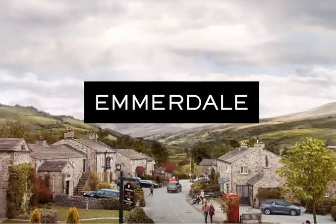 Casey Al-Shaqsy as Serena Sugden stands in a leather jacket against a stone wall in an Emmerdale scene.