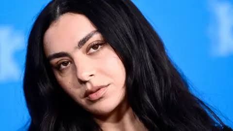 Charli XCX with dark hair looking directly at the camera in a close-up portrait.