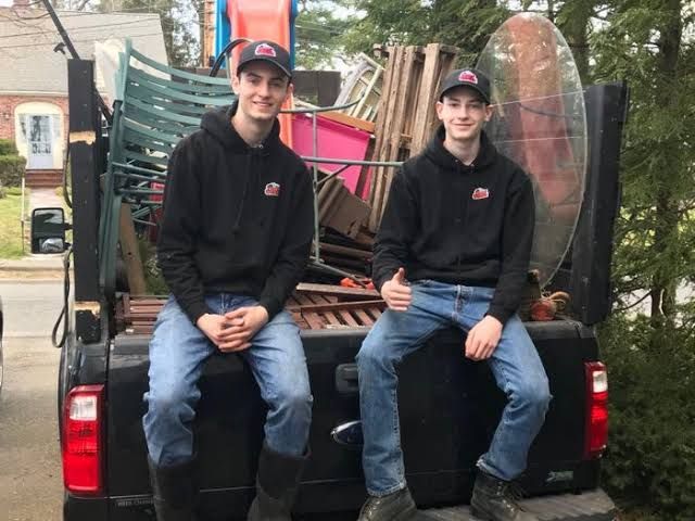 Kirk and Jacob McKinney standing in front of their branded junk removal dump truck.